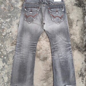 K&ouml;nnte beinhalten: Verblasste graue Jeans mit klassischem F&uuml;nf-Taschen-Design. Zu den Merkmalen geh&ouml;ren rote N&auml;hte an den Ges&auml;&szlig;taschen und ein Used-Look. Die Jeans hat einen geraden Bein-Schnitt und einen Knopf- und Rei&szlig;verschluss.