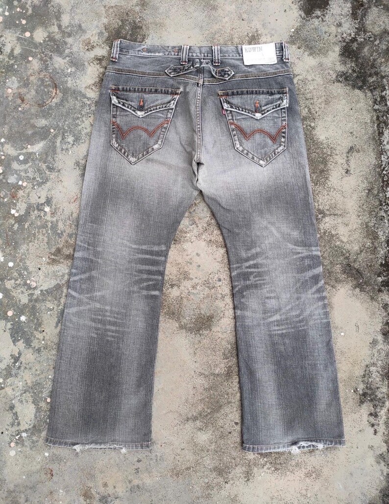 K&ouml;nnte beinhalten: Verblasste graue Jeans mit klassischem F&uuml;nf-Taschen-Design. Zu den Merkmalen geh&ouml;ren rote N&auml;hte an den Ges&auml;&szlig;taschen und ein Used-Look. Die Jeans hat einen geraden Bein-Schnitt und einen Knopf- und Rei&szlig;verschluss.