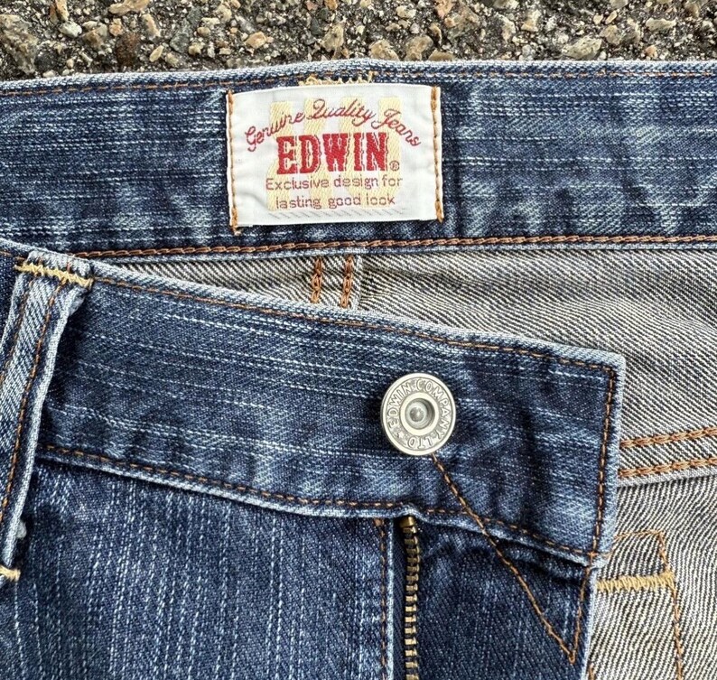 May include: Close-up of blue denim jeans with a button and zipper. A rectangular label reads "Genuine Quality Jeans EDWIN Exclusive design for lasting good look."