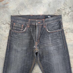 Pu&ograve; includere: Jeans in denim grigio scuro con cuciture e dettagli delle tasche arancioni. I jeans hanno un classico design a cinque tasche e una chiusura con bottoni. Il nome del marchio "XUS" &egrave; visibile in vita.