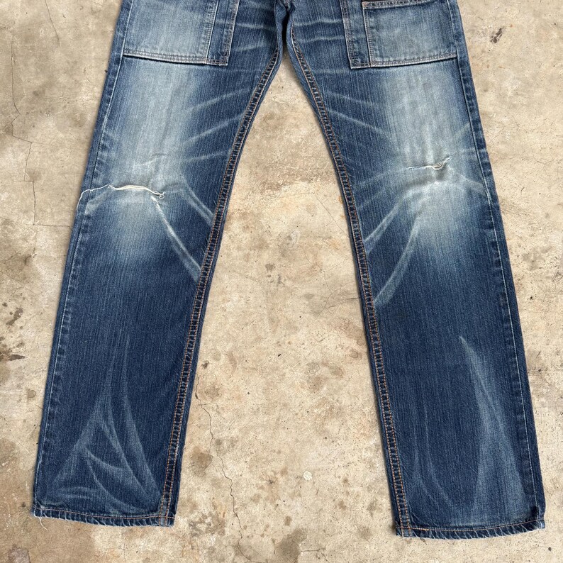 Op de afbeelding: Verbleekte blauwe denim jeans met een distressed look. De jeans hebben een klassiek vijf-zakken ontwerp, met twee voorzakken, twee achterzakken en een klein muntzakje. De jeans hebben een rechte pijp en zijn licht versleten bij de knie&euml;n.