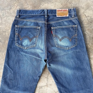 May include: Blue denim jeans with a classic five-pocket design. The jeans feature a faded wash, visible stitching, and a red tag on the back pocket. The brand name "EDWIN" is visible on a tag at the waistband.