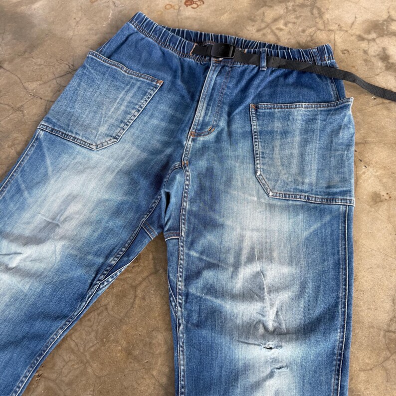 May include: Faded blue denim pants with a black belt. The pants have large, square pockets and a distressed look with a few small tears. The waistband is elasticized.