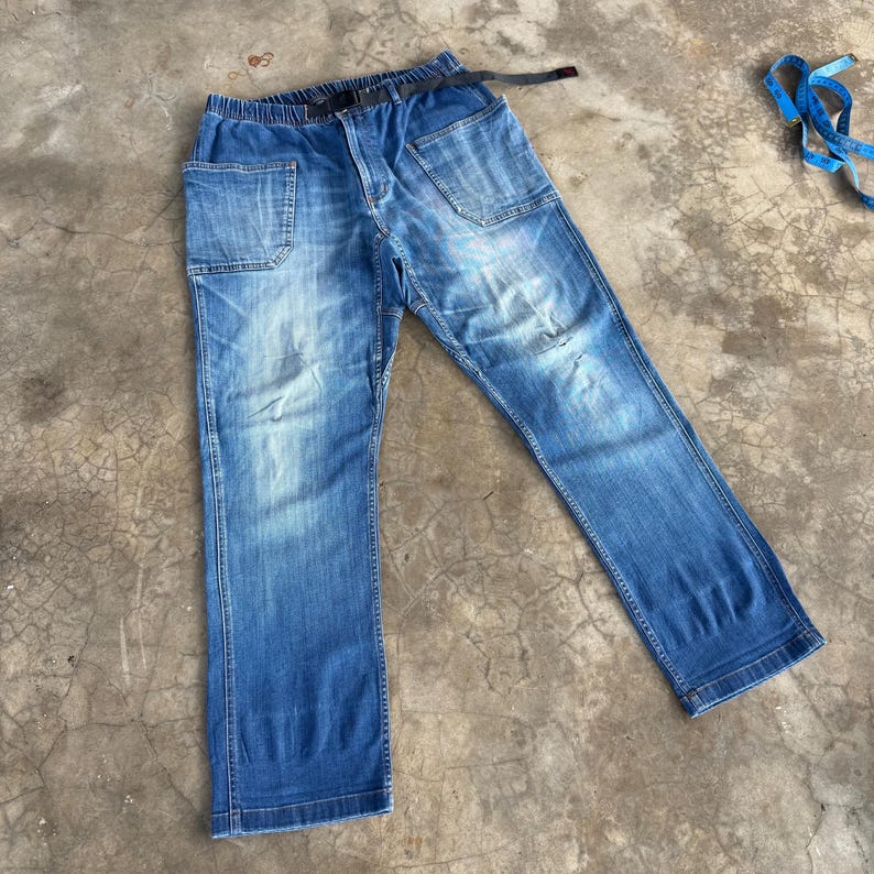 May include: Blue denim pants with a black belt. The pants have multiple pockets, a faded wash, and a relaxed fit. The pants are made of a durable denim material.