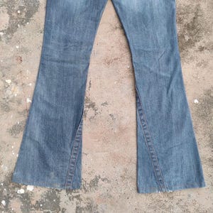 May include: A trio of cream-glazed ceramic mugs with a speckled finish. Each mug is adorned with a hand-painted design: a blue and green leaf, a yellow flower, and a red berry. The mugs have a simple, modern design.