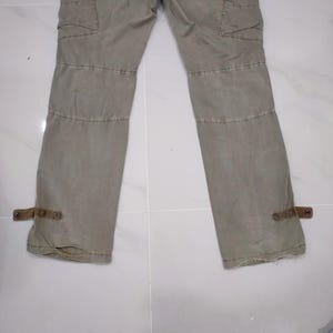 May include: Khaki-colored cargo pants with multiple pockets and stitched details. The pants have reinforced knee panels and adjustable straps at the ankles. The fabric appears to be a durable, medium-weight material.