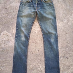 May include: Faded blue denim jeans with a button fly and classic five-pocket design. The jeans show signs of wear and fading, with a straight leg cut. The denim has a vintage, worn-in look.