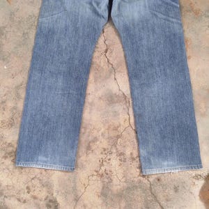 May include: Light blue denim jeans with a classic straight leg cut. The jeans show signs of wear and fading, with a medium wash. The image is a top-down view of the jeans.