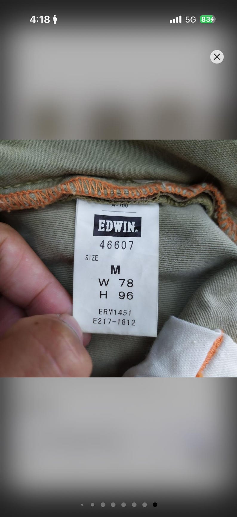 May include: Close-up of a tag from Edwin jeans. The tag is white with black text, displaying the brand name, size M, and measurements: W 78 inches, H 96 inches. The tag is sewn into olive green fabric.