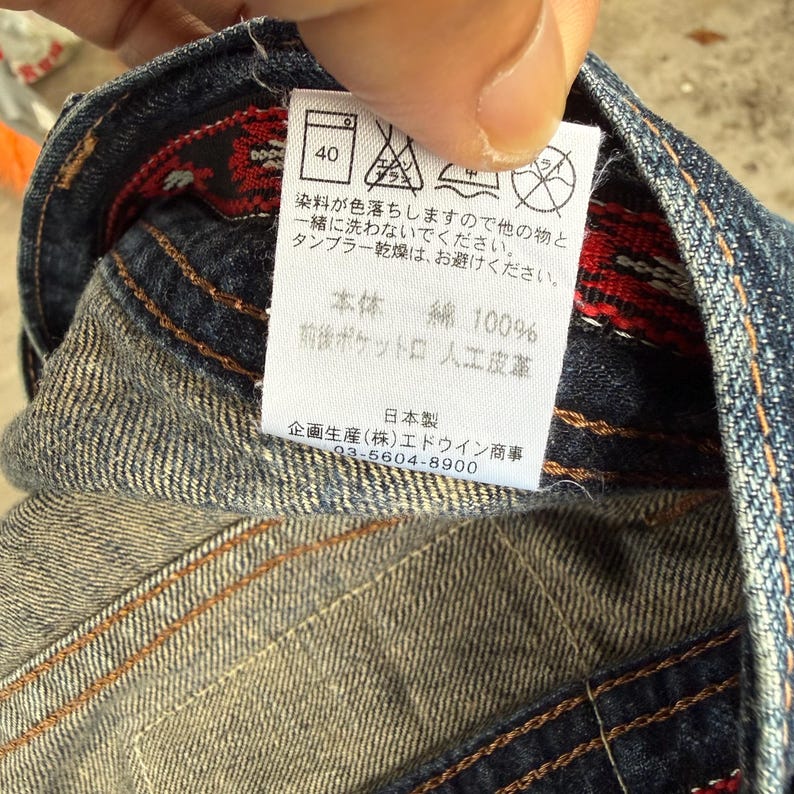 Op de afbeelding: Close-up van een denim kledinglabel met Japanse tekst en verzorgingssymbolen. Het label geeft wasvoorschriften en geeft aan dat het kledingstuk van 100% katoen is. Het label heeft ook het nummer 40.