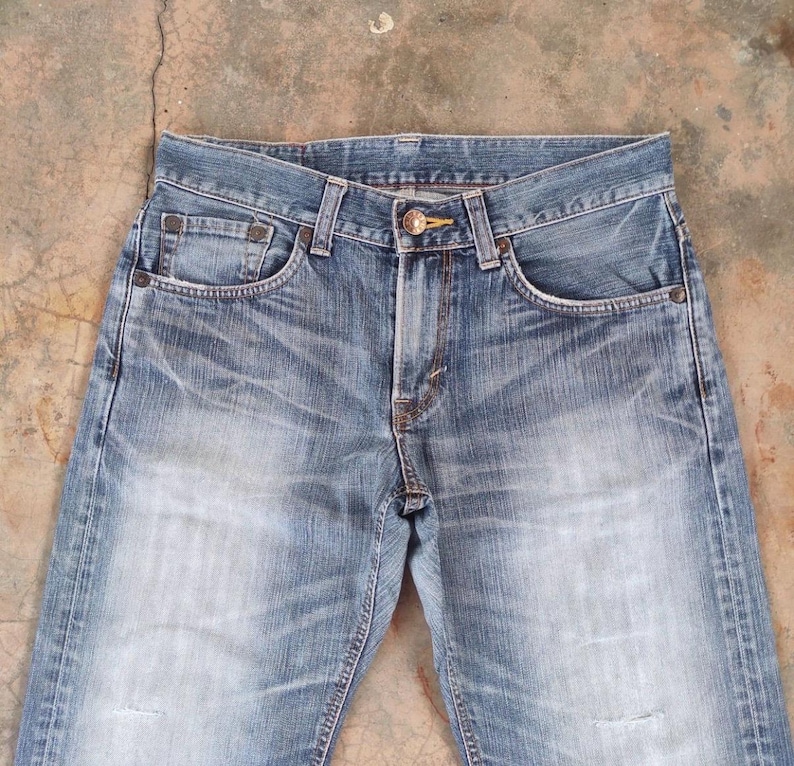 May include: Light blue denim jeans with a faded wash and distressed details. The jeans feature classic five-pocket styling, a button and zipper closure, and belt loops. The denim has a worn appearance.