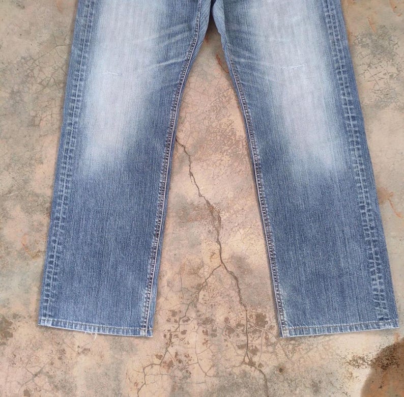 May include: Faded blue denim jeans with a straight leg cut. The jeans have a classic five-pocket design and a button and zipper closure. The denim has a worn look with lighter areas on the thighs and knees.