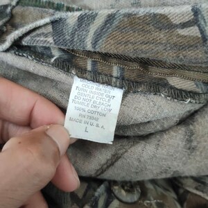 May include: Close-up of a camouflage-patterned fabric with a care label. The label reads "MACHINE WASH COLD WATER TURN INSIDE OUT GENTLE CYCLE DO NOT BLEACH TUMBLE DRY LOW 100% COTTON RN 73342 MADE IN U. S. A. L".