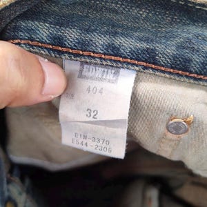 May include: Close-up of a denim jeans label with the brand name "EDWIN" at the top. The label shows the size "32" and style number "404". Additional numbers and letters are also visible on the label.