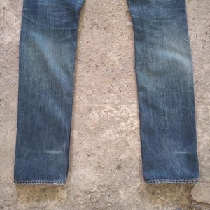 May include: Faded blue denim jeans. The jeans have a straight leg cut and show signs of wear and fading, particularly around the knees and thighs. The denim has a classic, vintage look.