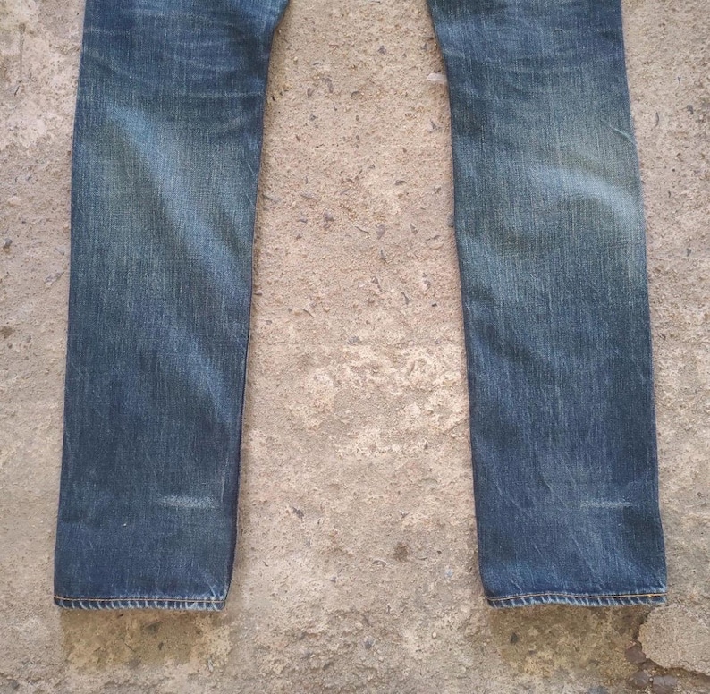 May include: Faded blue denim jeans. The jeans have a straight leg cut and show signs of wear and fading, particularly around the knees and thighs. The denim has a classic, vintage look.