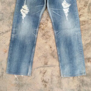 May include: Light blue denim jeans with distressed detailing. The jeans feature ripped sections on the front of the legs, creating a worn and vintage aesthetic. The denim has a faded appearance, adding to the casual style.