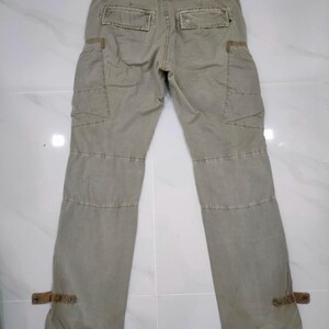 May include: Khaki-colored cargo pants with multiple pockets and reinforced stitching. Features include two back pockets, two side pockets, and decorative straps at the ankles. The pants are made of a durable fabric.