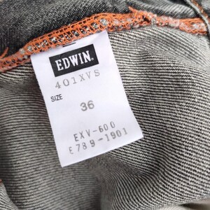 K&ouml;nnte beinhalten: Nahaufnahme eines Jeans-Kleidungsst&uuml;ck-Etiketts. Das wei&szlig;e Etikett zeigt die Marke "EDWIN" und die Gr&ouml;&szlig;e "36". Der Jeansstoff ist grau mit sichtbaren orangefarbenen N&auml;hten.