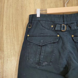 Pu&ograve; includere: Pantaloni blu navy scuro con cintura e finiture color oro. I pantaloni hanno due grandi tasche sul retro e una piccola tasca sul davanti. I pantaloni sono appesi a un'appendiabiti di legno.