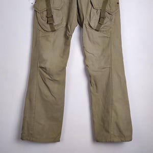 May include: Khaki-colored cargo pants with large pockets and straps. The pants have a relaxed fit and are made of a durable material. The design includes reinforced knees and a straight leg.