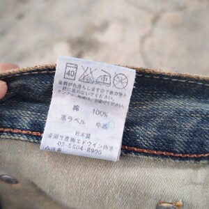 May include: Close-up of a denim garment with a white tag. The tag displays washing instructions, Japanese text, and the number "40". The tag also indicates the material is 100% cotton and has a leather label.