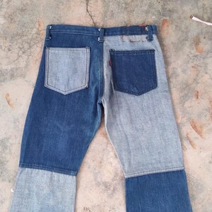 May include: Two-tone denim jeans with a patchwork design. The jeans feature a mix of light and dark blue denim panels, with a classic five-pocket design. The back pockets are visible, and a red tag is on one pocket.