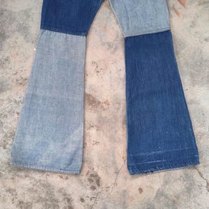 May include: A pair of patchwork denim jeans with a flared leg design. The jeans are constructed from two different shades of blue denim, creating a color-blocked effect. The jeans are laid flat, showcasing the full length and style.