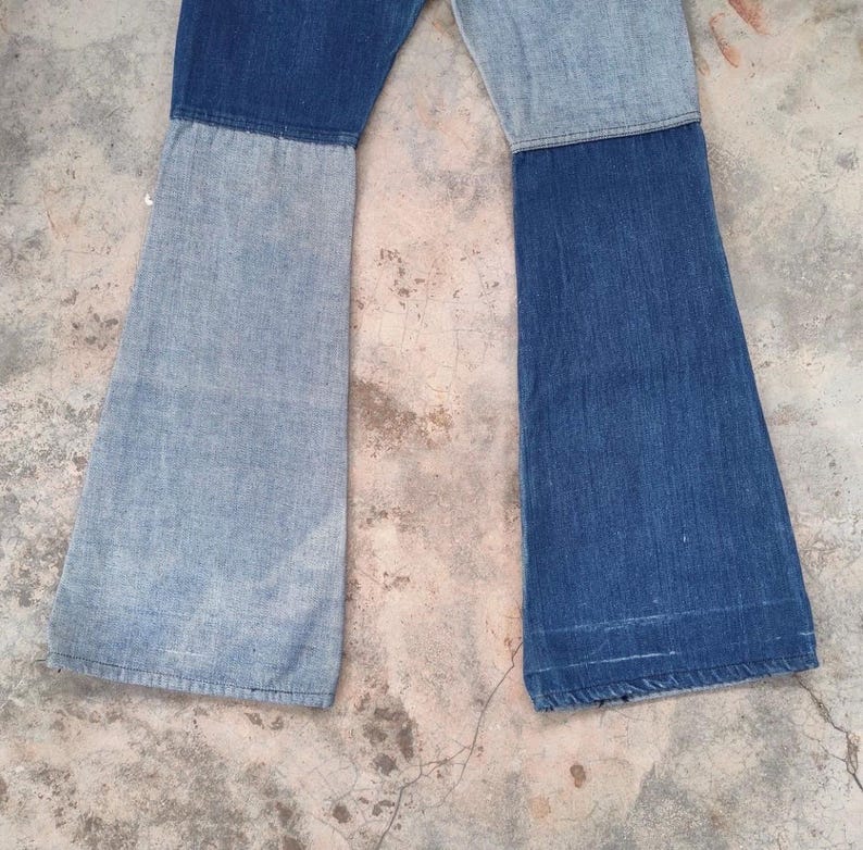 May include: A pair of patchwork denim jeans with a flared leg design. The jeans are constructed from two different shades of blue denim, creating a color-blocked effect. The jeans are laid flat, showcasing the full length and style.