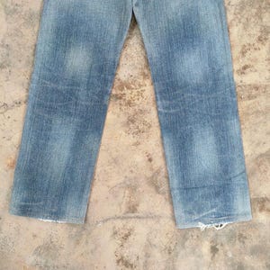May include: Light blue denim jeans with a faded wash and distressed hem. The jeans have a classic five-pocket design and a straight leg fit. The fabric shows signs of wear, adding to the vintage aesthetic.