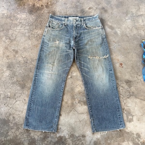 Puede incluir: Vaqueros de mezclilla azul descolorido con un aspecto desgastado. Los vaqueros tienen un dise&ntilde;o cl&aacute;sico de cinco bolsillos, bragueta con botones y un corte relajado. Hay varios rasgu&ntilde;os y roturas en los vaquero, d&aacute;ndoles una apariencia vintage.