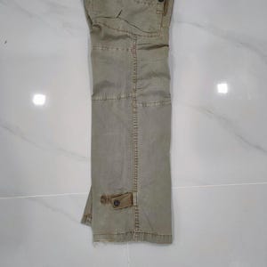 May include: Khaki-colored cargo pants with multiple pockets and a button closure. The pants are made of a durable fabric and have a relaxed fit. The pants are folded and displayed on a white surface.