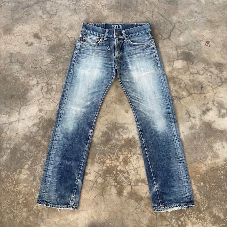 May include: Faded blue denim jeans with a button fly and the number "503" printed on the waistband. The jeans have a classic five-pocket design and show signs of wear and fading, giving them a vintage look.
