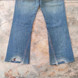 May include: Light blue denim jeans with a flared leg design. The jeans feature a split seam detail on the outer leg and distressed detailing at the hem. The jeans are faded and show signs of wear.