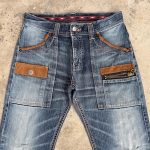 Op de afbeelding: Blauwe spijkerbroek met bruine su&egrave;de-achtige accenten op de zakken en decoratieve stiksels. Voorzien van een knoopsluiting en een zak met ritssluiting. De jeans heeft een vervaagde wassing en een patroon in de tailleband.