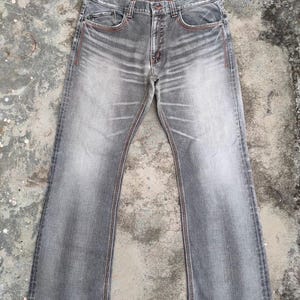 K&ouml;nnte beinhalten: Graue Jeans mit verwaschener Optik und leicht ausgestelltem Bein. Die Jeans hat rote N&auml;hte an den S&auml;umen und Taschen. Sie hat ein klassisches F&uuml;nf-Taschen-Design und einen Knopf- und Rei&szlig;verschluss.