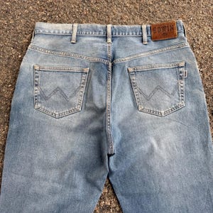 May include: Light blue denim jeans with a classic five-pocket design. Features a brown leather patch with the brand name "EDWIN" on the back waistband. The back pockets have a distinctive stitched design. The jeans are made of a durable denim fabric.