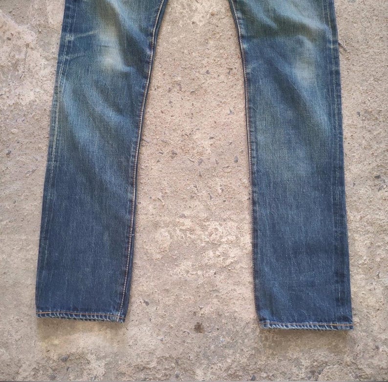 May include: A pair of faded blue denim jeans. The jeans have a straight leg cut and show signs of wear and fading, particularly around the knees and thighs. The denim has a classic five-pocket design.