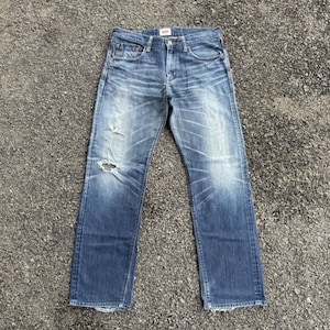 May include: Faded blue denim jeans with a distressed look, featuring a ripped knee and light wash details. The jeans have a classic five-pocket design and a straight leg fit.