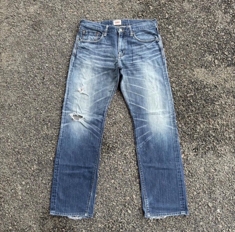 May include: Faded blue denim jeans with a distressed look, featuring a ripped knee and light wash details. The jeans have a classic five-pocket design and a straight leg fit.