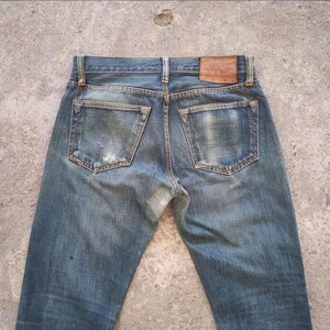 May include: Faded blue denim jeans with a worn appearance. The jeans feature two back pockets, a leather patch, and visible wear and tear. The jeans are a classic style.