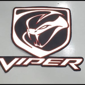 May include: A black and white Viper logo patch with a red border. The patch features a snake head design within a shield shape, and the word "VIPER" below it.