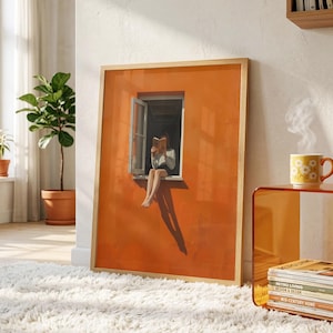 May include: A framed art print depicts a person reading in a window against an orange wall. The artwork is in a light wood frame and is placed on a white fluffy rug. A yellow mug with a floral design sits on a side table.