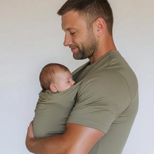 Peut inclure: Un porte-b&eacute;b&eacute; enveloppant vert olive maintient un nourrisson endormi. Le porte-b&eacute;b&eacute; est int&eacute;gr&eacute; dans un t-shirt vert olive assorti. L'image montre un gros plan du b&eacute;b&eacute; et du t-shirt.