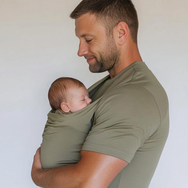 Peut inclure: Un porte-b&eacute;b&eacute; enveloppant vert olive maintient un nourrisson endormi. Le porte-b&eacute;b&eacute; est int&eacute;gr&eacute; dans un t-shirt vert olive assorti. L'image montre un gros plan du b&eacute;b&eacute; et du t-shirt.