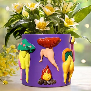 May include: A purple ceramic planter with whimsical mushroom and leg designs in yellow, green, pink, and red. The planter holds a vibrant arrangement of white and yellow flowers with green foliage, creating a colorful and artistic display.