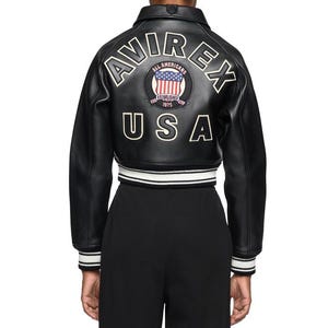 K&ouml;nnte beinhalten: Eine wei&szlig;e Keramik-Tasse mit schwarzem Henkel und dem Text "But First, Coffee" in fetter, schwarzer Schrift. Die Tasse steht vor einem verschwommenen Hintergrund, der eine gem&uuml;tliche Umgebung suggeriert.