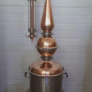 May include: A copper and stainless steel still with a bulbous body, a conical top, and a coiled condenser. The still has a shiny, reflective surface and is designed for distilling. The still is approximately 76 cm tall.