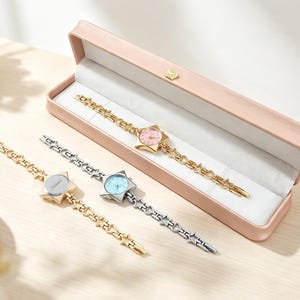 Peut inclure: Trois montres-bracelets en forme d'étoile avec des maillons à motifs d'étoiles. Une montre dorée au cadran rose est dans un boîtier rectangulaire rose. Deux autres montres, une dorée au cadran vierge et une argentée au cadran bleu, sont posées à côté.