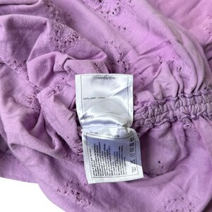 May include: A light purple, short-sleeved shirt with a textured design and a gathered waist. The shirt has a tag that reads "COMPOSITION" and "100% coton / cotton".